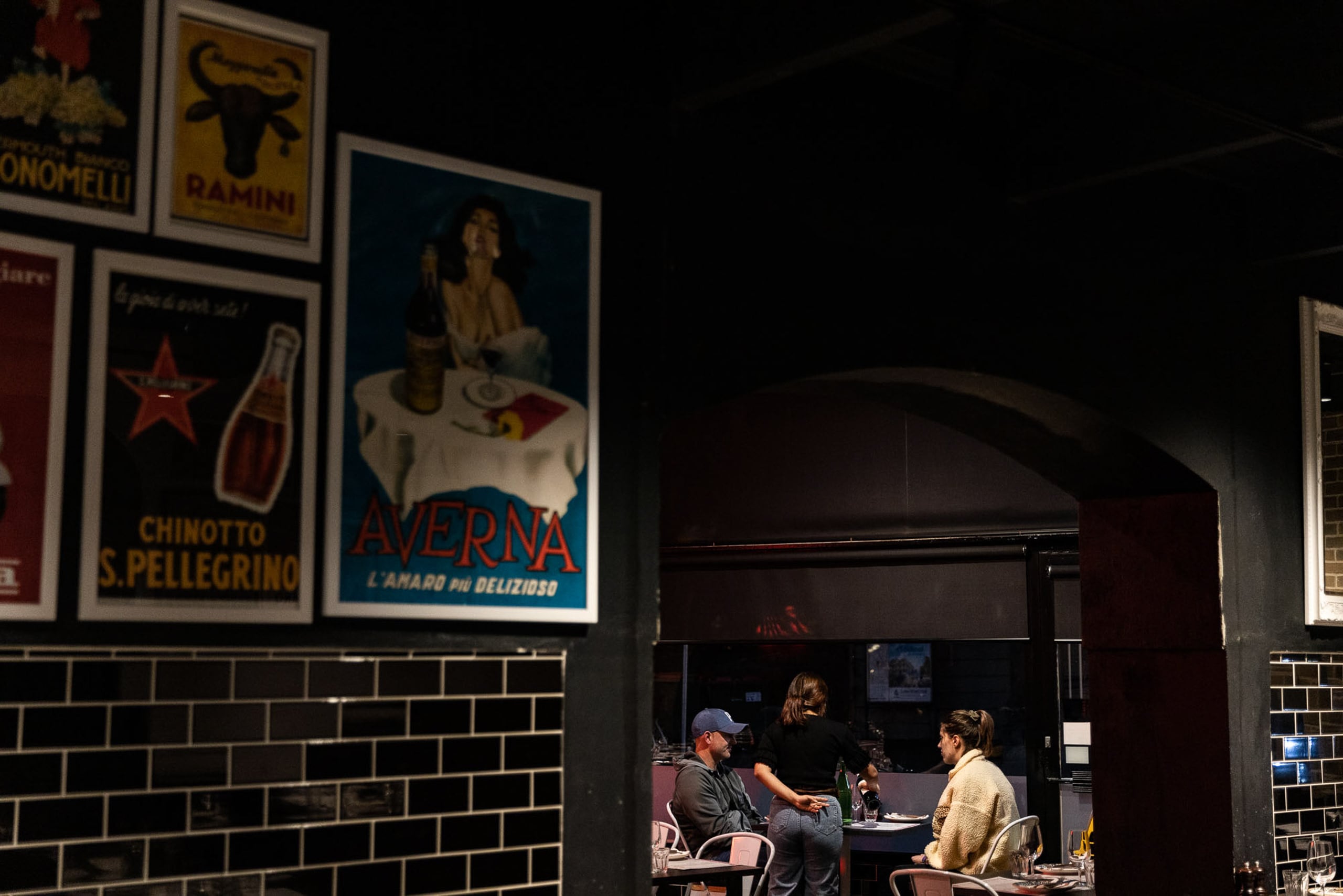 The inside of an Italian restaurant. A image hangs on the wall and people sit around a table in the background.